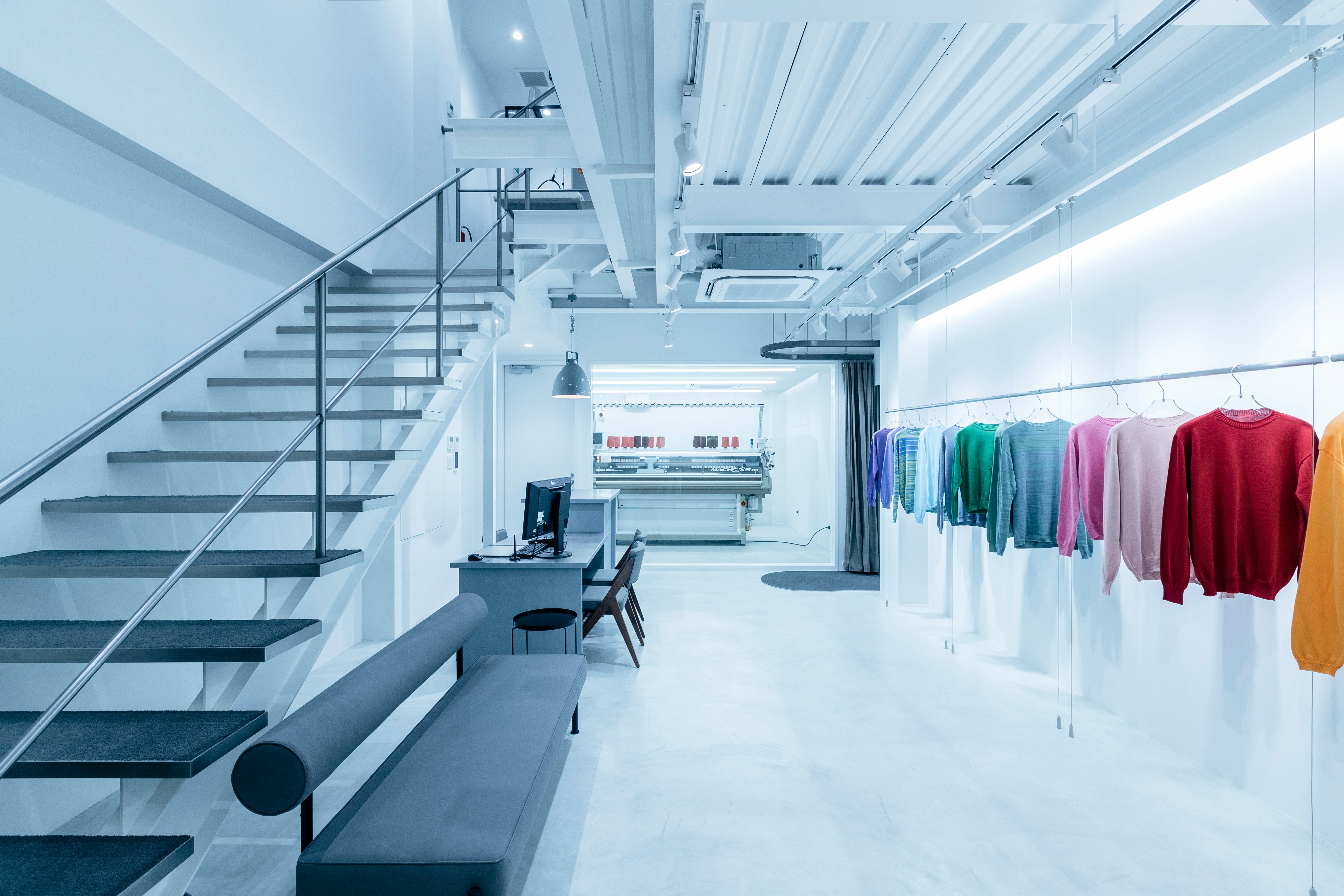 完成した色とりどりの服のラックと、奥の編み機が見える岡山の店舗兼ファクトリー